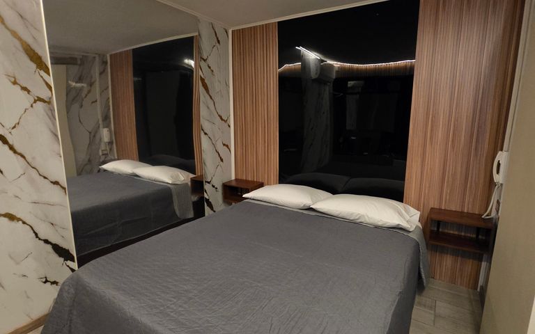 Habitación de Motel Match con piso de madera, cama de dos plazas, espejo y televisión